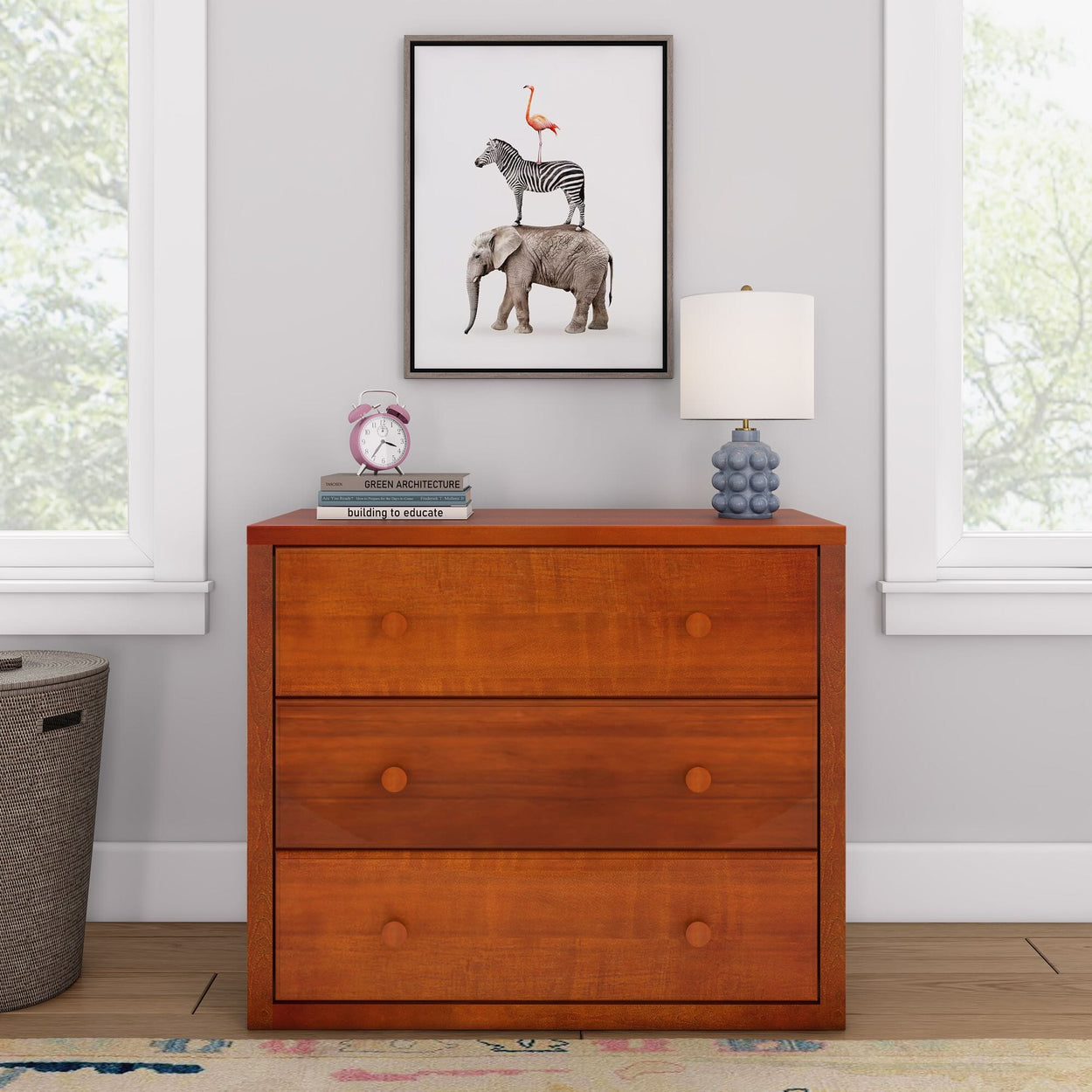 Wooden dresser with drawers, modern bedroom decor featuring a whimsical animal stack art print, lamp, and vintage alarm clock.