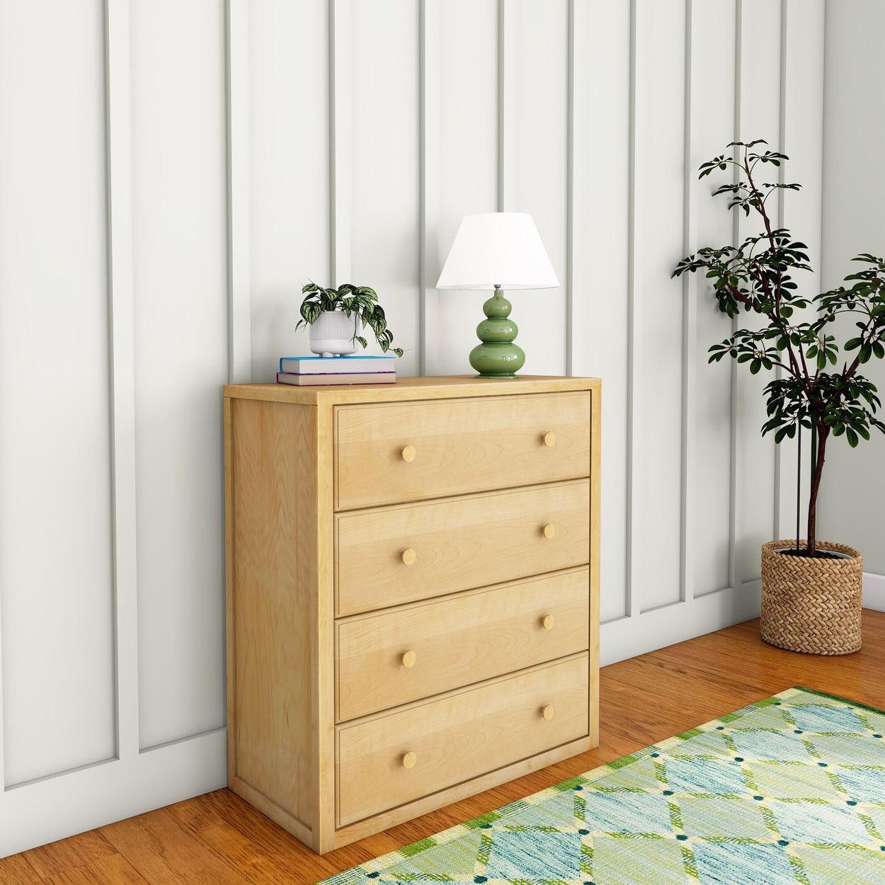 Wooden dresser with four drawers, green lamp, potted plant, and wall paneling in cozy room setting.