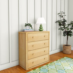 Wooden dresser with four drawers, green lamp, potted plant, and wall paneling in cozy room setting.