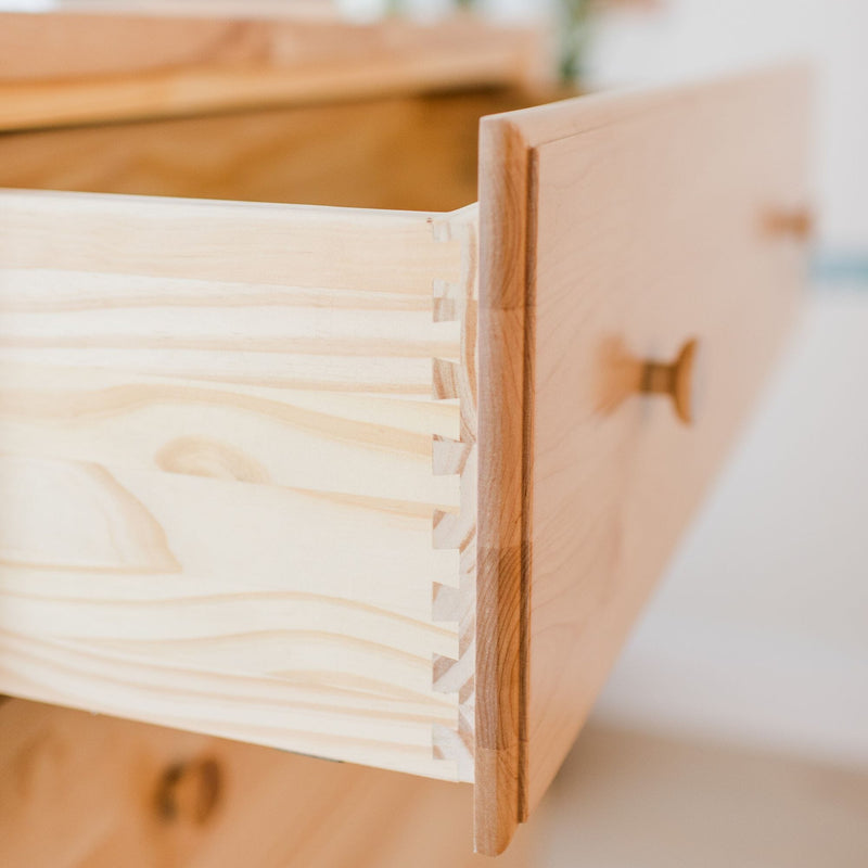 Close-up of dovetail joint on light pine drawer — precision woodworking joinery for handmade wooden furniture and cabinet drawers