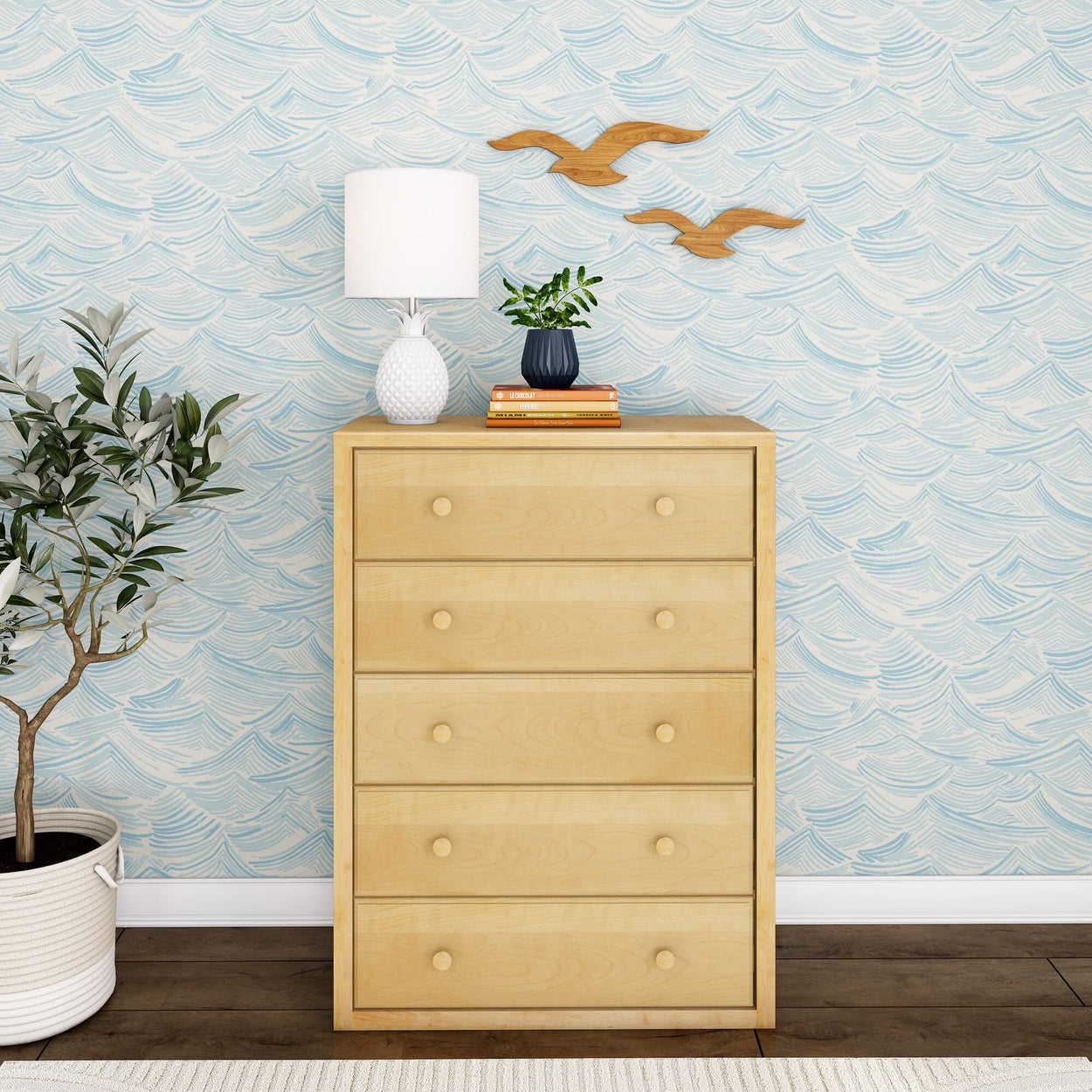 Wooden dresser with four drawers beside a plant and modern decor against a wave-patterned wallpaper in a stylish room.