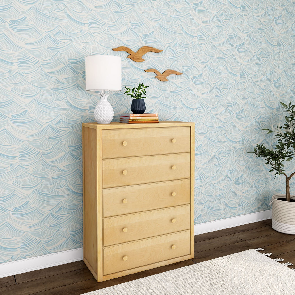 Wooden dresser with a white lamp and plant, in a room with wave-patterned wallpaper.