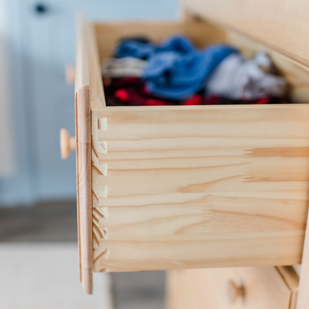 Open wooden dresser drawer with clothes inside.