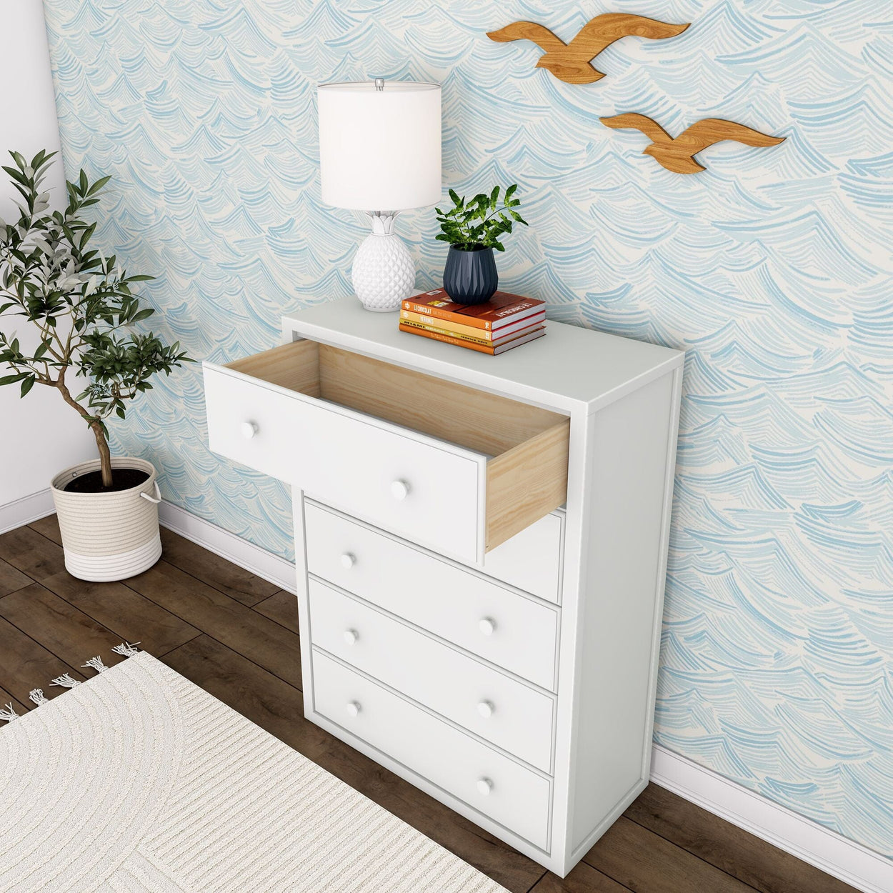 White chest of drawers with an open drawer, next to a potted plant and a white lamp, against a blue wave-patterned wallpaper.