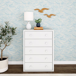 White dresser with lamp and plant in modern interior design featuring wave-patterned wallpaper.
