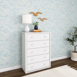 White dresser with lamp and plant against blue patterned wallpaper in modern bedroom.