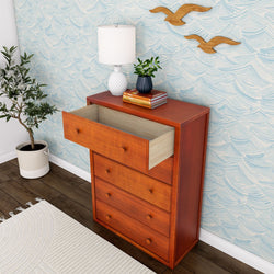 Wooden dresser with open drawer and decorative items, featuring a patterned wall background and potted plant.