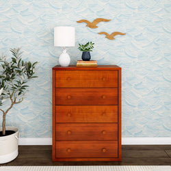 Stylish wooden dresser with four drawers against a wave-patterned wall, featuring a lamp and plant decor, enhancing modern home interior design.