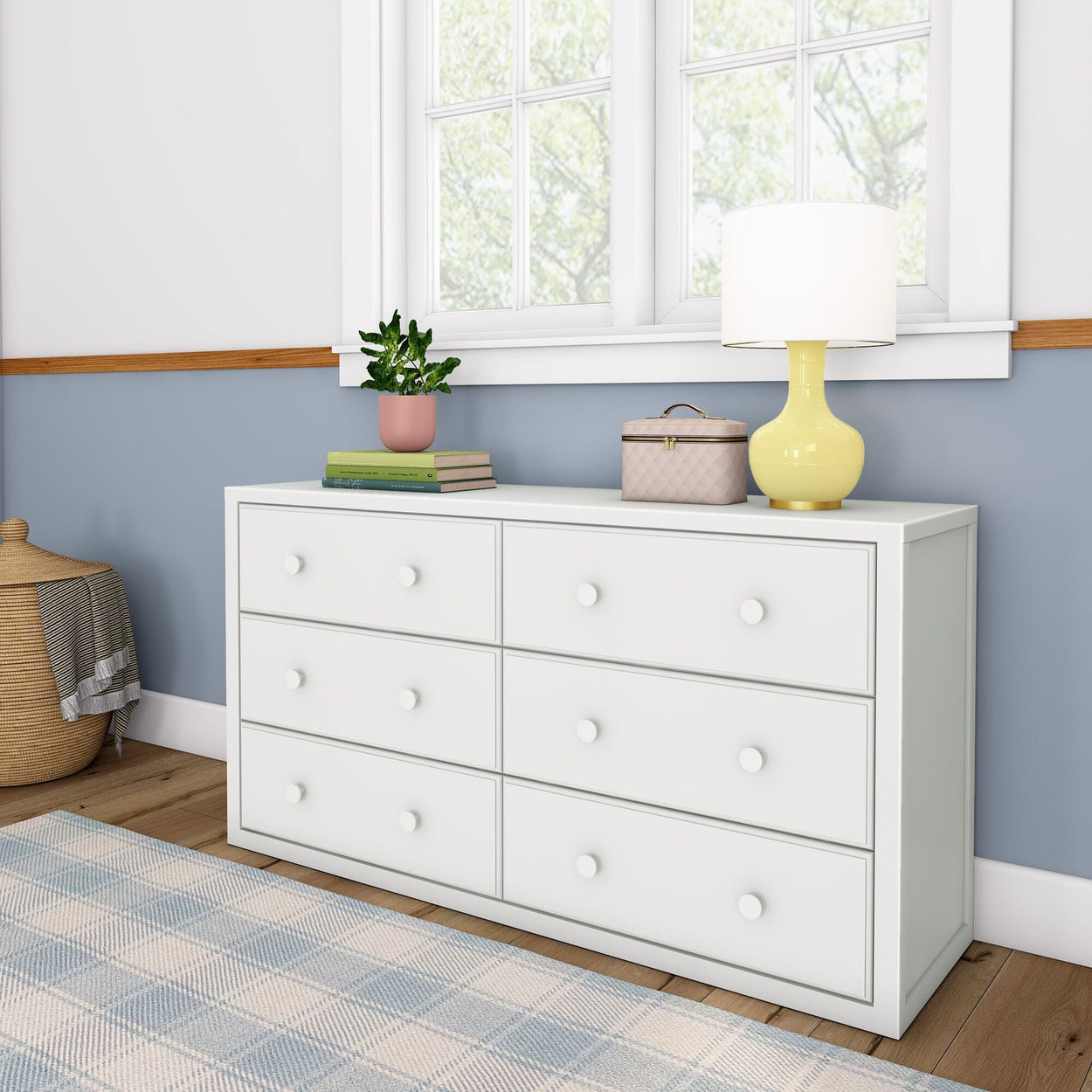White six-drawer dresser with yellow lamp, books, and plant in a modern bedroom.