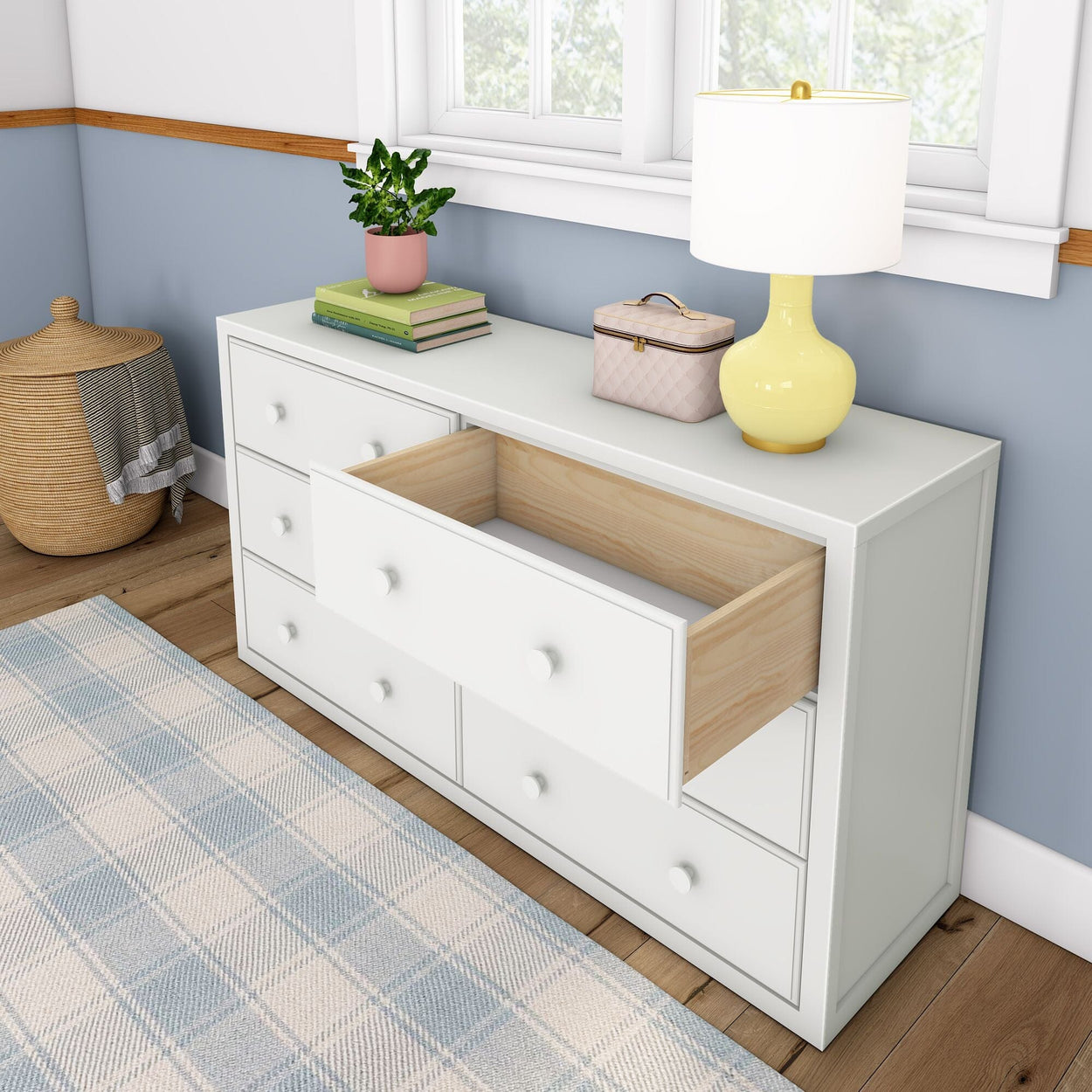 White dresser with an open drawer, lamp, books, plant, and decorative basket in a modern bedroom setting.