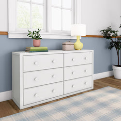 White six-drawer dresser with decorative items, including a yellow lamp and potted plants, in a modern bedroom setting.