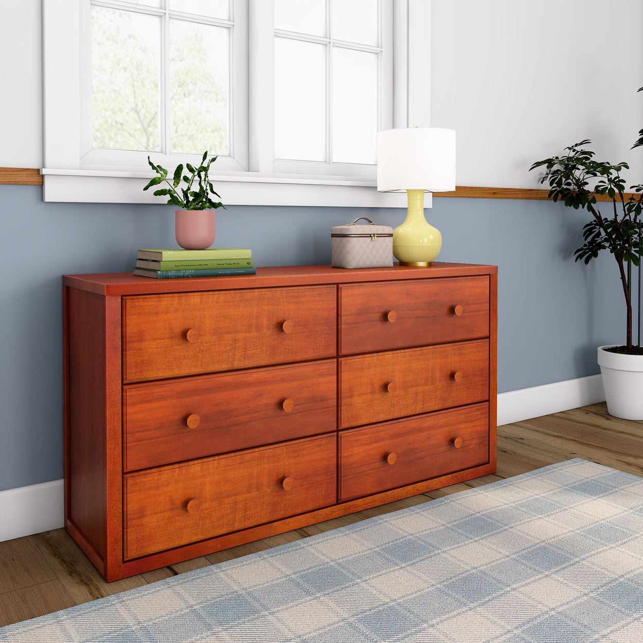 Wooden dresser with six drawers in a cozy room with a lamp and potted plants.