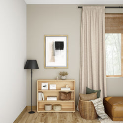 Minimalist living room with a wooden bookshelf, black floor lamp, and abstract wall art, featuring beige curtains and a cozy seating area.
