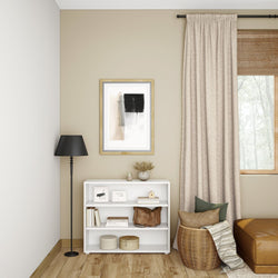 Stylish living room corner with modern decor, including a black floor lamp, abstract wall art, beige curtains, and a white shelf with decorative items.