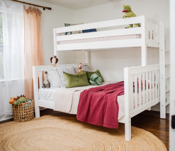 A light natural wood children's loft bed with an attached desk and storage drawers, shown in a bright, modern bedroom setting.