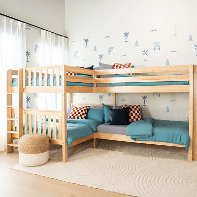 A light natural wood twin-size desk with three drawers, styled next to a wooden bunk bed and a matching wooden chair with a white seat in a bright room.