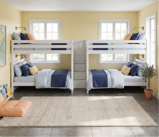 Modern kids' bedroom with white twin over-twin bunk beds featuring central staircase and built-in drawers, navy blue and white bedding, yellow walls, large windows, beige area rug and potted plant.