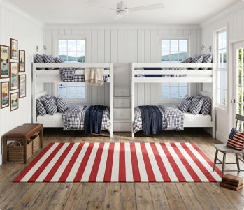 Modern kids' bedroom with white twin over-twin bunk beds featuring central staircase and built-in drawers, navy blue and white bedding, yellow walls, large windows, beige area rug and potted plant.