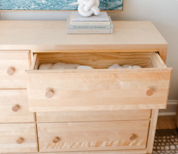 Light wood dresser with an open drawer filled with folded white towels, coastal bedroom decor featuring a decorative knot sculpture and ocean art print