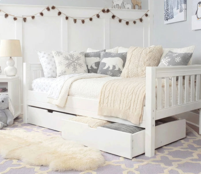White wooden daybed with under-bed storage drawers in a cozy kids' bedroom nursery, winter-themed polar bear and snowflake pillows, cream cable-knit throw, shag rug and pinecone garland.