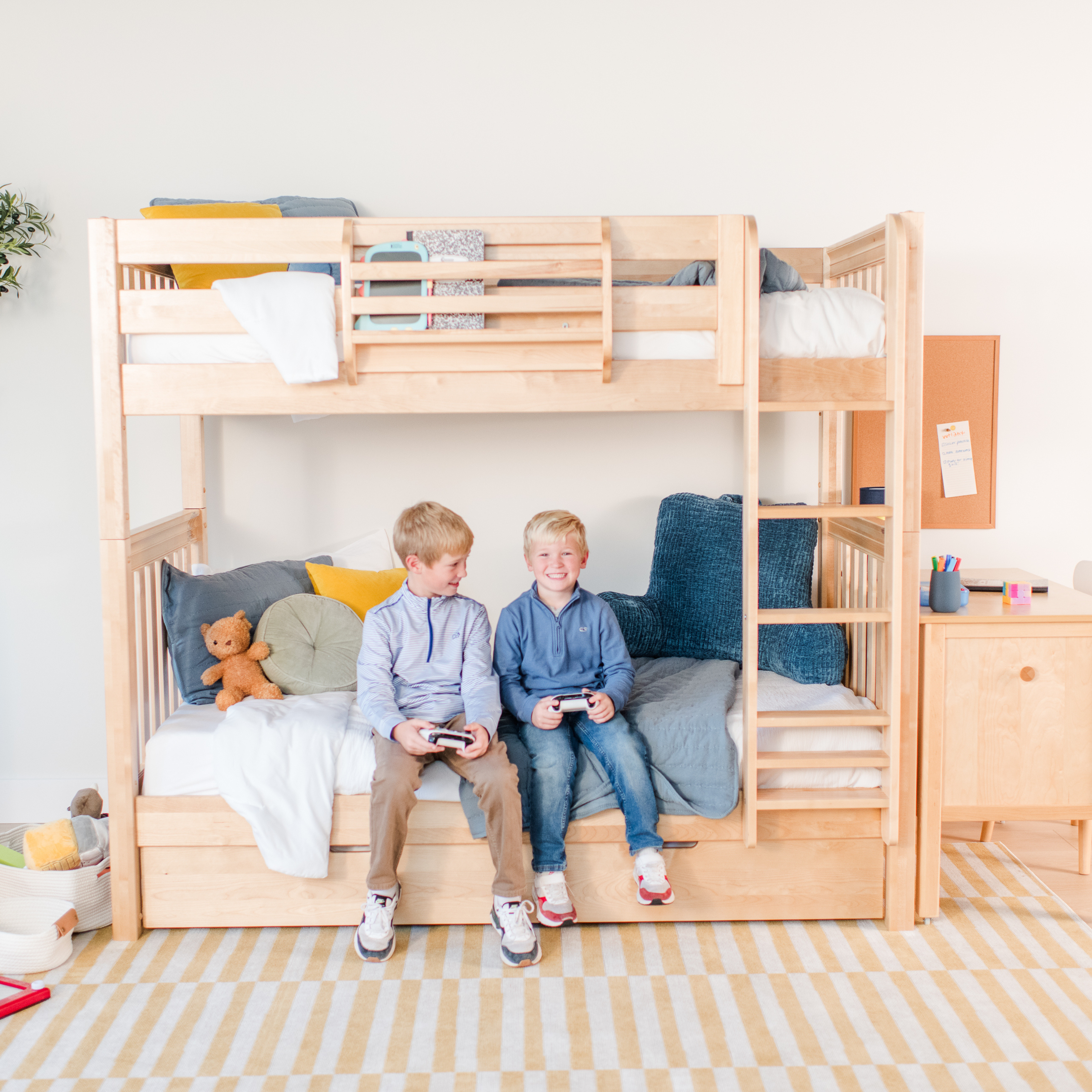 A light natural wood children's loft bed with an attached desk and storage drawers, shown in a bright, modern bedroom setting.