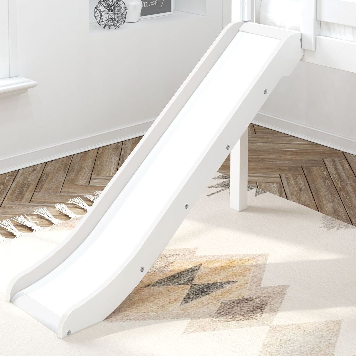 White wooden slide attached to a modern indoor kids' bunk bed, placed on a geometric patterned rug in a bright room.
