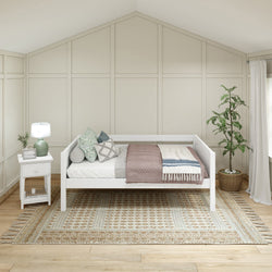 Daybed with decorative pillows in a modern, neutral-tone bedroom featuring a woven area rug and potted plant.