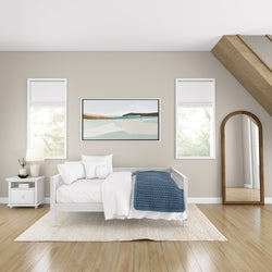 Modern minimalist bedroom with white daybed, blue throw blanket, framed wall art, and wooden accents.