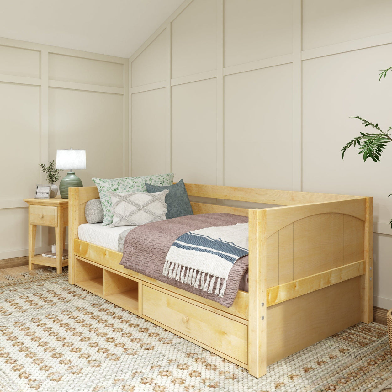 Cozy modern bedroom with natural wood daybed and storage drawers, decorated with textured pillows and blanket, next to a wooden nightstand and green potted plant.