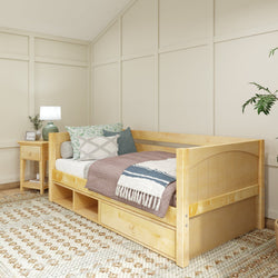 Cozy modern bedroom with natural wood daybed and storage drawers, decorated with textured pillows and blanket, next to a wooden nightstand and green potted plant.