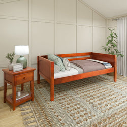 Wooden daybed with decorative pillows in a cozy bedroom interior featuring a bedside table with a lamp and a striped area rug.