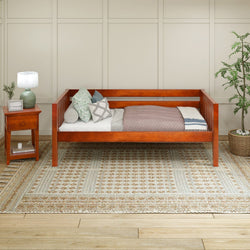 Stylish wooden daybed with decorative pillows, cozy blanket, and a side table with a lamp in a modern minimalist bedroom setting.