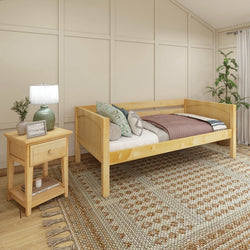 Cozy bedroom with a wooden daybed, patterned rug, and nightstand featuring a lamp and decorative plant.