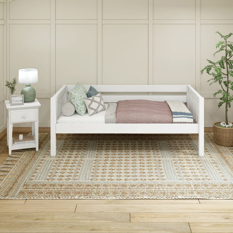 White wooden daybed with patterned pillows and mauve throw on a textured neutral area rug, next to a white nightstand with green lamp and potted plant, cozy Scandinavian bedroom decor