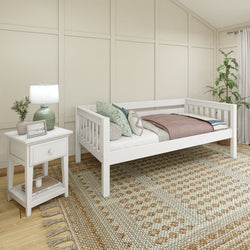 White daybed in a cozy bedroom with wooden nightstand, patterned area rug, and decorative pillows.