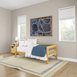 Contemporary bedroom interior with wooden bed frame, white bedding, and navy blue blanket, featuring abstract wall art and natural light from windows.
