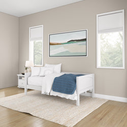 Modern minimalist bedroom with white bed, blue blanket, soft natural lighting, and abstract wall art.