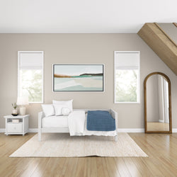 Modern minimalist bedroom with white bed, blue throw blanket, framed wall art, and wooden floor mirror.