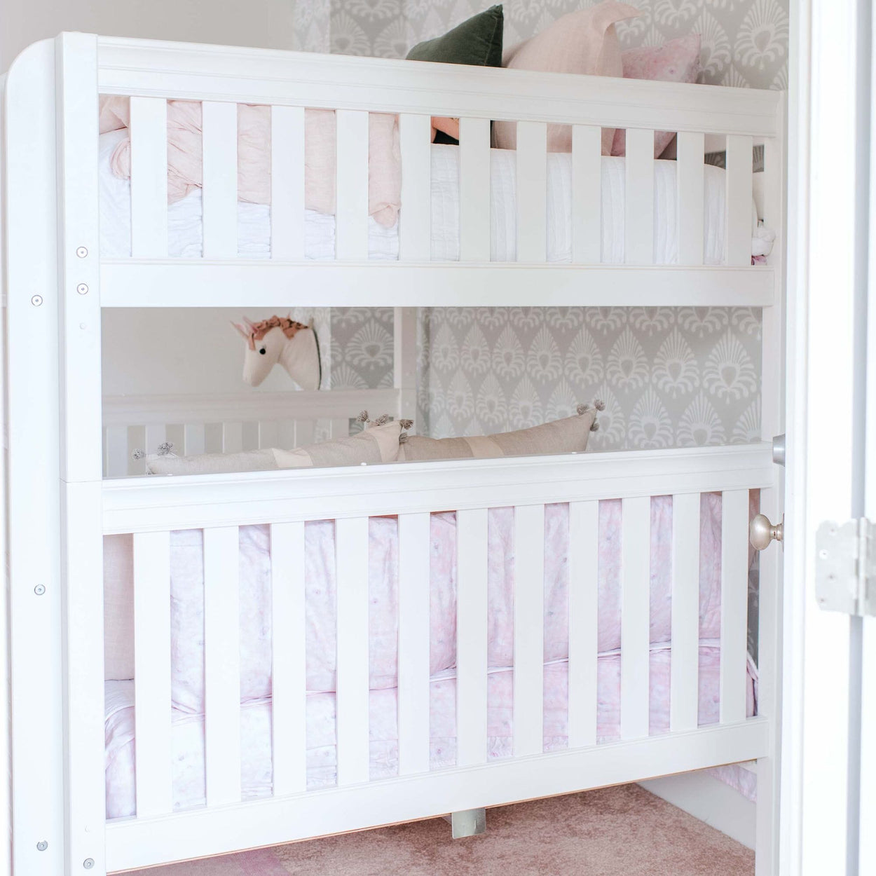 White wooden bunk bed with pink bedding and a decorative unicorn head mounted on the light gray patterned wall in a cozy children's bedroom.