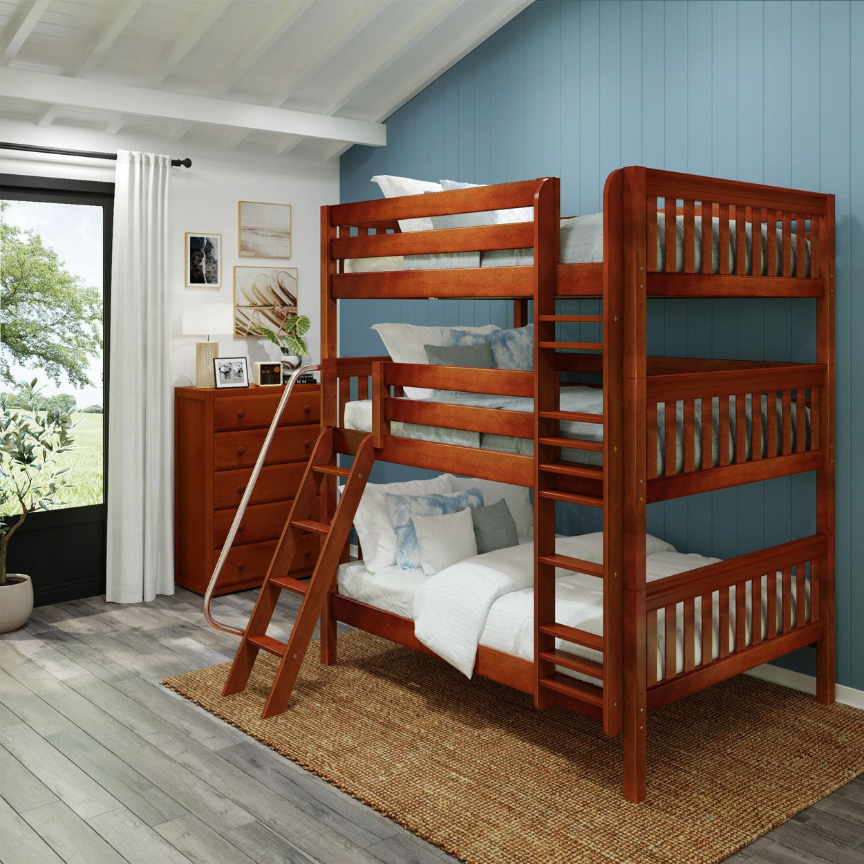 Wooden triple bunk bed in a modern bedroom with blue accent wall and natural light from a large window.