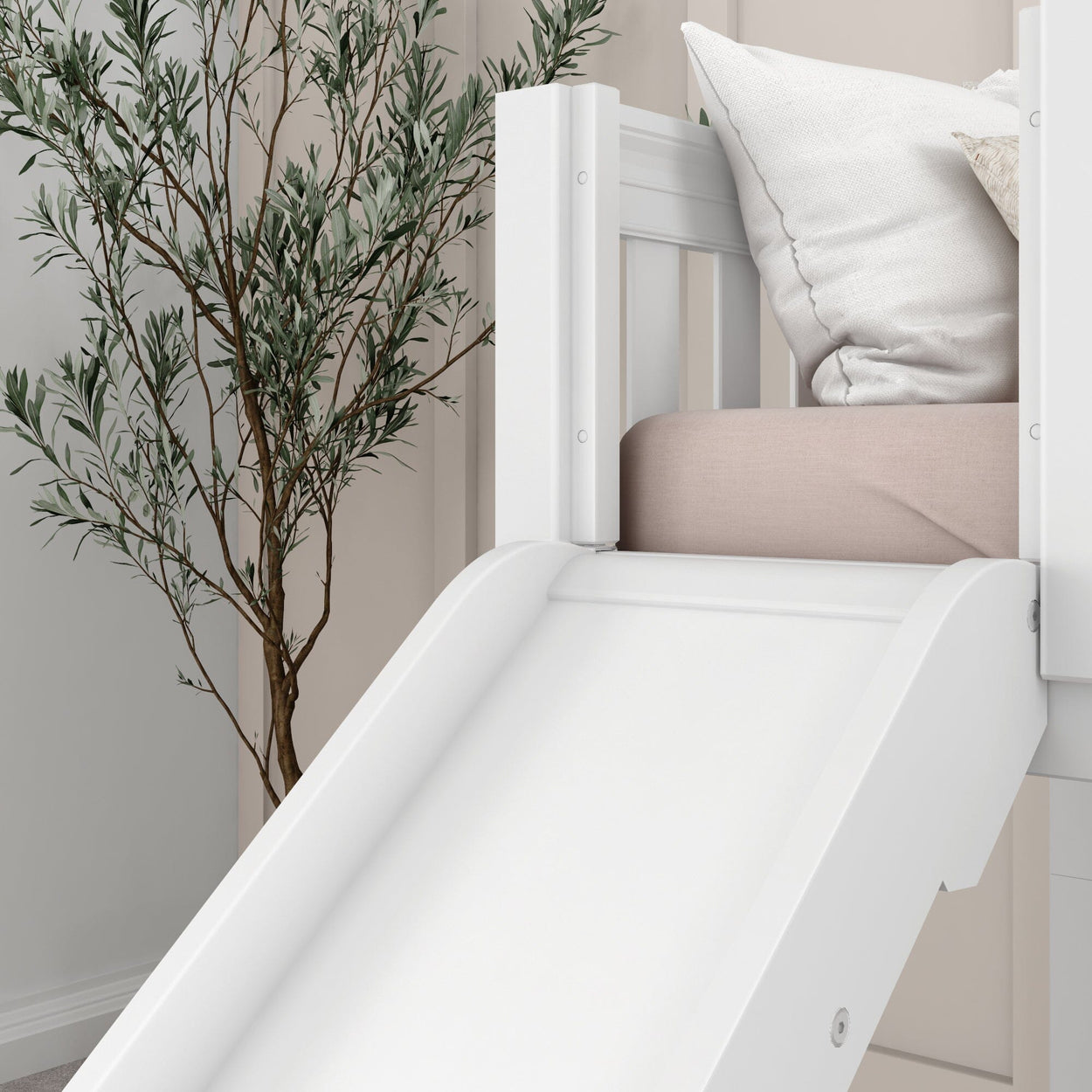 White children's bed with an indoor slide and pillows, next to a green plant.