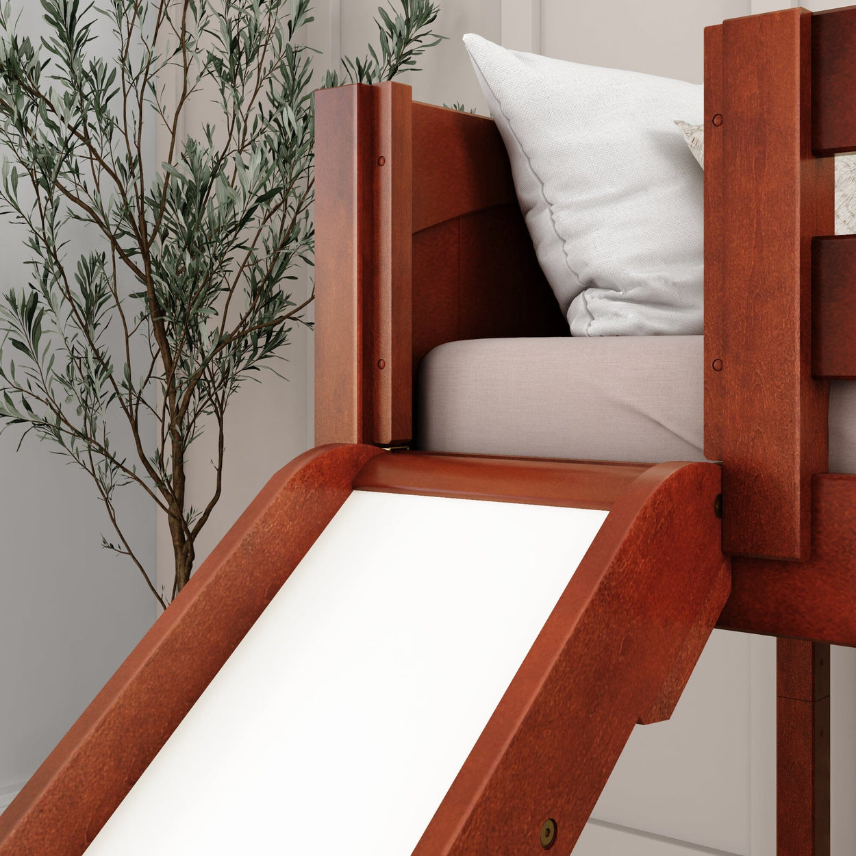 Wooden children's bed with a slide and cozy pillows next to a potted plant in a modern bedroom.