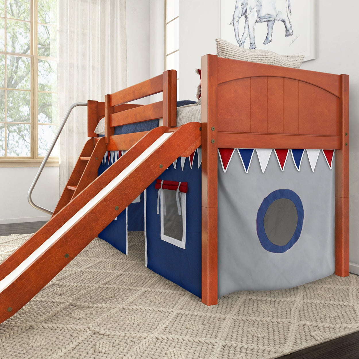 Wooden kids bunk bed with slide and tent-style play area underneath, featuring nautical-themed decor in a bright bedroom setting.