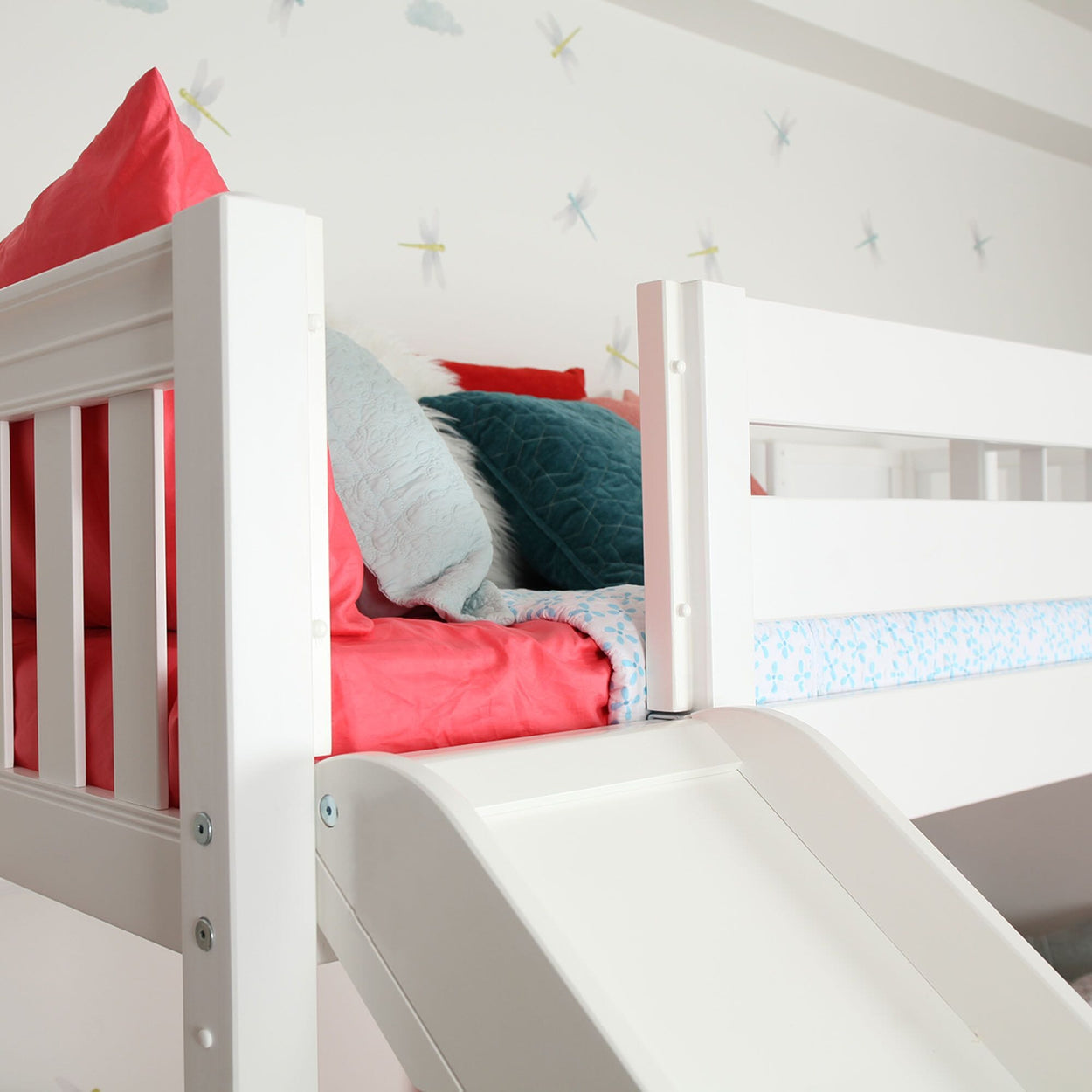 Children's white loft bed with colorful pillows and a slide in a playful bedroom setting.