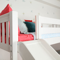 Children's white loft bed with colorful pillows and a slide in a playful bedroom setting.