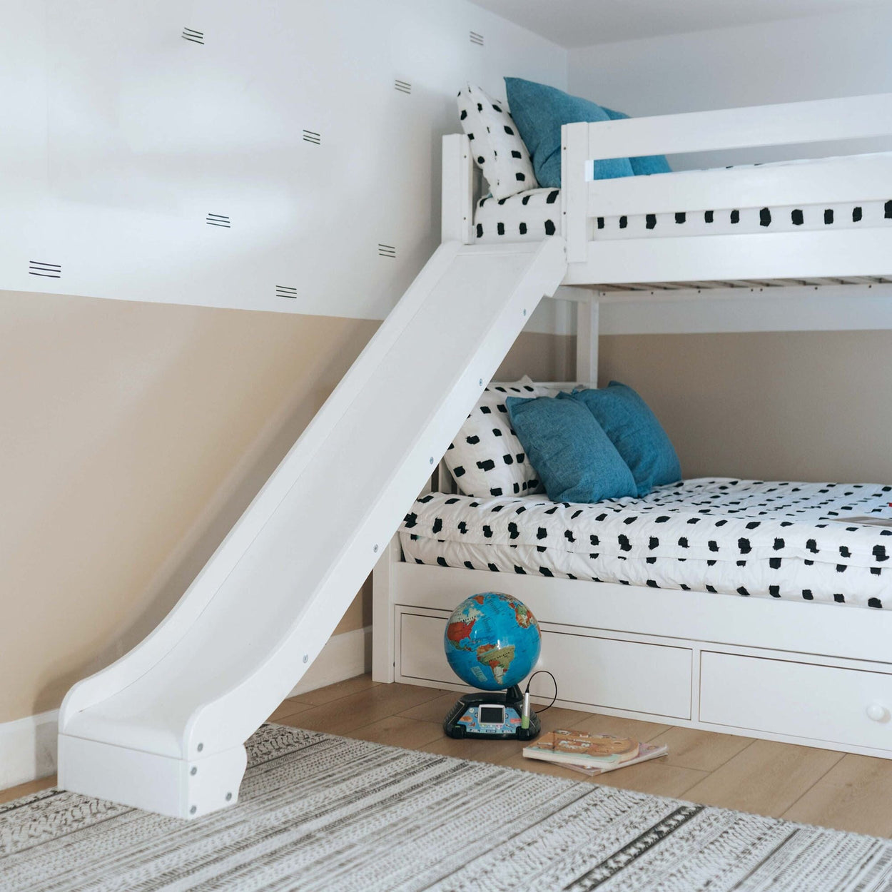 Kids' white bunk bed with slide, blue cushions, and polka dot bedding in modern children's room.