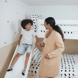 Mom and child playing indoors on a bunk bed slide in a cozy bedroom setting.