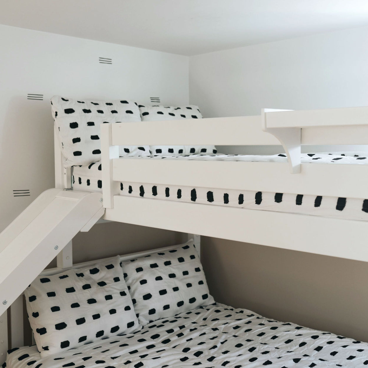 White bunk bed with black and white polka dot bedding, ideal for kids' room decor.