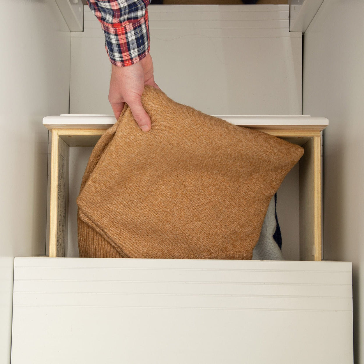 Hand placing a cozy brown sweater in a drawer for organized storage.