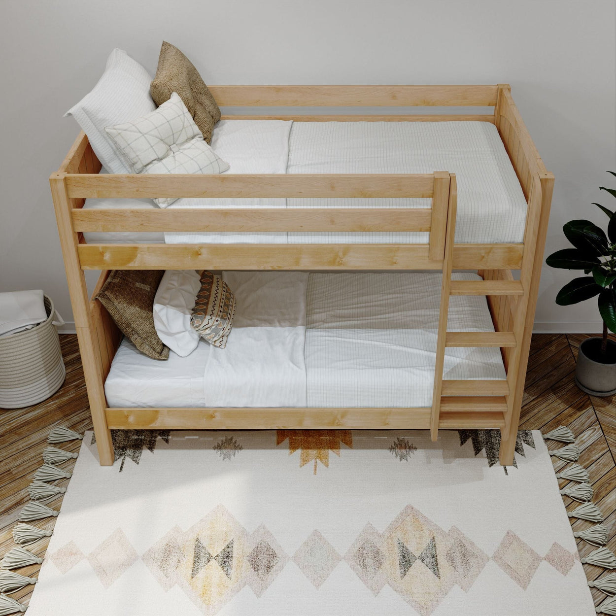 Wooden bunk bed with white bedding and decorative pillows, placed on a patterned rug near a potted plant in a cozy bedroom setting.